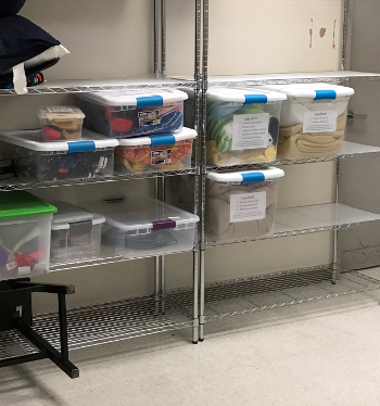 Lab equipment is stored in plastic containers on shelves in the 3T suite