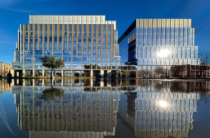 Aggie Square building with its reflection in a pool of water below. 
