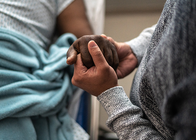 Holding hands with a patient in a hospital bed.