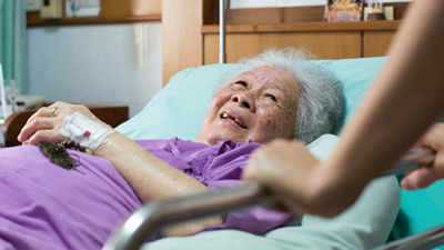 A smiling woman spiritually comforted by a chaplain in her hospital room.