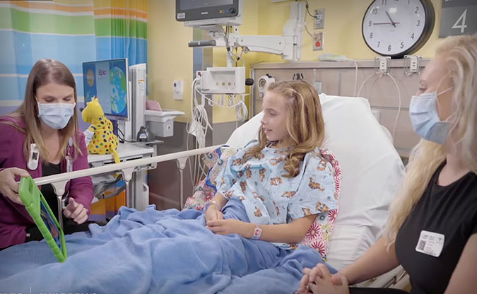 Patient with child life specialist and mom in a hospital bed