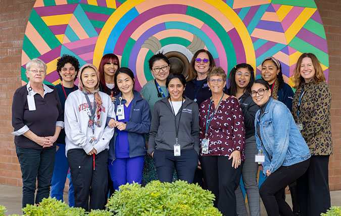 CIRCLE Clinic Team, 13 members, pose in front of circular colorful design on building mural