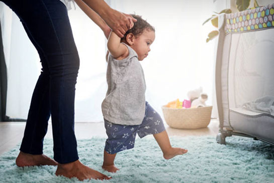 Baby taking first step with mom holding hands