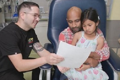 Man in black shirt shows paper to man and daughter