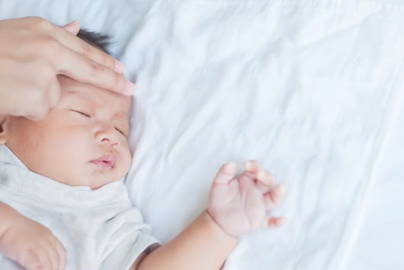 an infant with an adult's fingers on their forehead checking their temperature. 