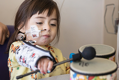 Small injured child in Physical Therapy playing with a drum.