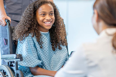 Young adolescent girl in wheelchair and hospital gown after procedure