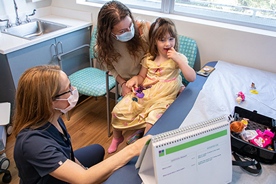 A healthcare worker with a mother and her child sitting in a room having a conversation.