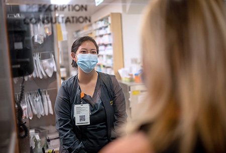 Pharmacist at a window consulting with a patient