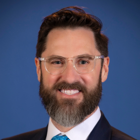 Mark Fedyk smiles with a beard and glasses while wearing a suit with a blue tie.