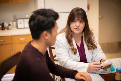 A woman doctor in a white coat sits next to a patient to talk.