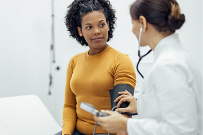 A woman patient in a sweater sits while listening to her doctor, a woman in a medical coat.