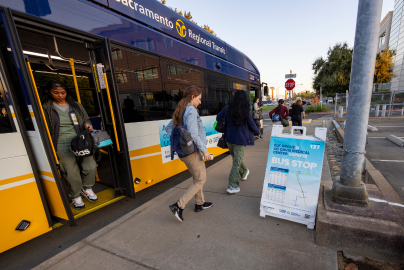 Commuters get off a bus stop in Elk Grove, CA near a UC Davis Health sign.