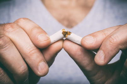 Two hands are seen breaking a cigarette in half. 