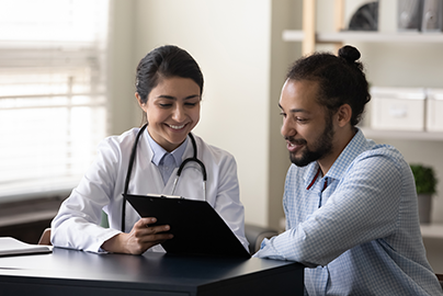 Doctor pointing to clipboard, talking to smiling patient.