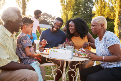 A multi-generational family eats a meal outdoors in a park. 