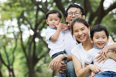 Family of four outside surrounded by trees smiling.