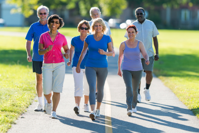 A group of diverse older adults exercise and walk through a park path surrounded by grass.