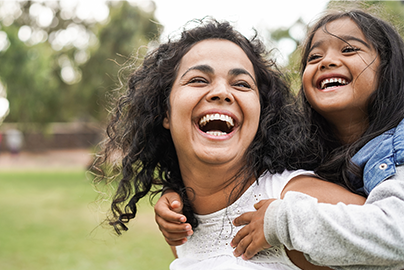 Mother and young daughter holding onto mom's back, smiling.