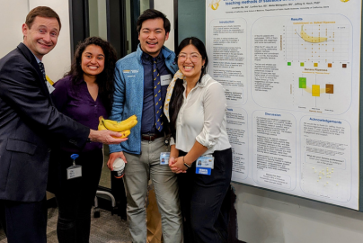 Jeffrey Hoch, UC Davis professor, holds bananas next to three medical students and their research poster.