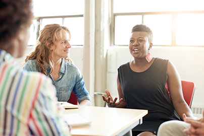 Woman talking to more people seated at a conference table.