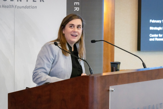Courtney Lyles, director of the Center for Healthcare Policy and Research, wears a grey coat while speaking behind a podium.