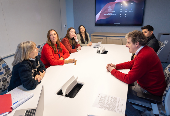 A team of six researchers sit around a table in discussion.