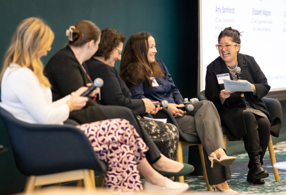 Five women seated for a panel discussion hold microphones.