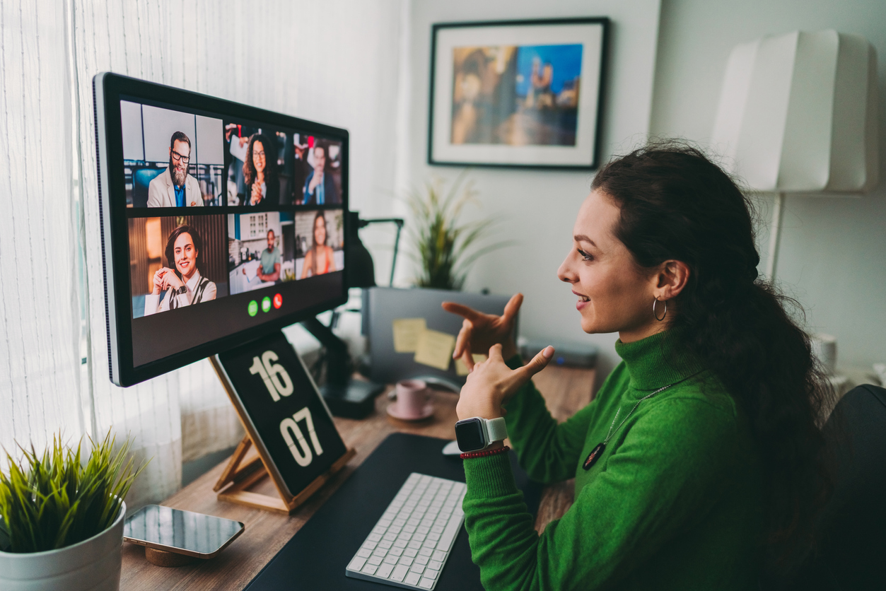 Person participating in a video call on a computer, gesturing while speaking to multiple people displayed on the screen.