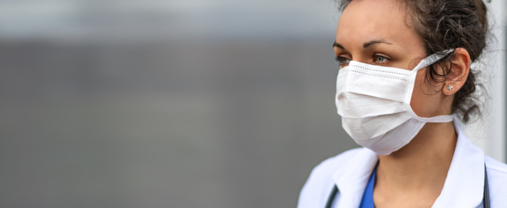 A woman doctor with curly hair looks to the side while wearing a face mask.