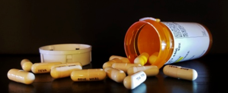 Pills spill out of a tipped over pill bottle on a dark background.