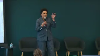 A woman in a dark suite speaks into a microphone.