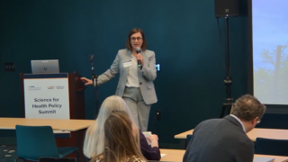 A woman in a suit speaks into a microphone.