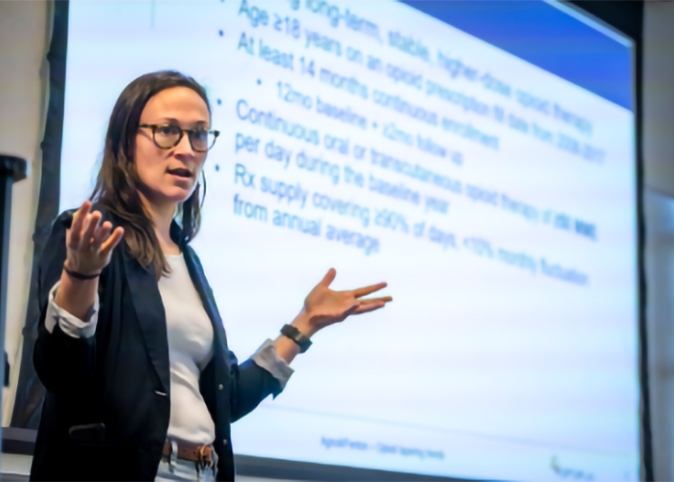 Professor Alicia Agnoli, wearing a black coat, speaks in front of a screen.