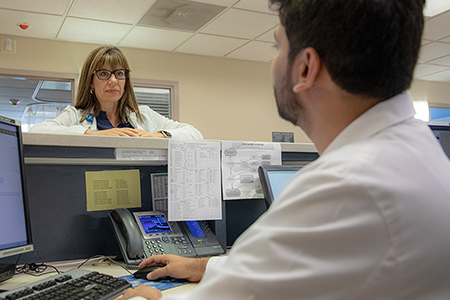 A doctor speaking to a healthcare worker at a work station.