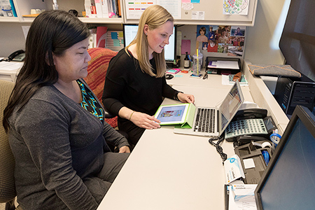 Two healthcare workers looking at computers working at a desk.
