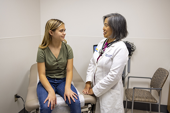 Teenage girl sitting on exam table smiling at female health care provider