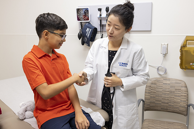 Teen boy shaking hands with health care provider while sitting on an exam table