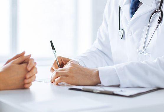 Close up of health professional’s hands resting on a table across from another person’s hands.