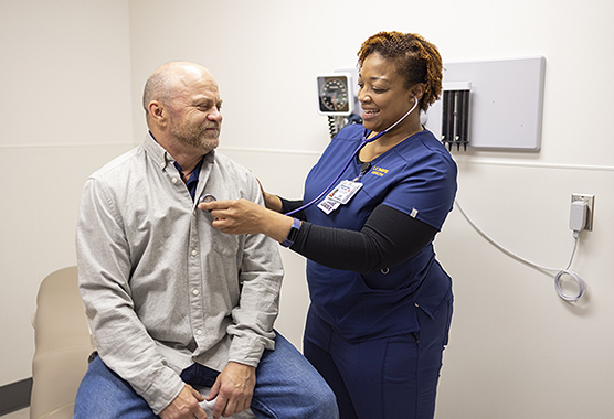 Female nurse listening to the heart of a male patient in an exam room with a stethoscope.