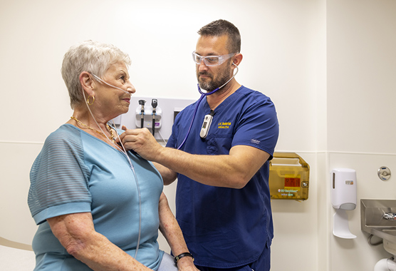 Health care provider listening to woman’s heart with stethoscope in clinic room.