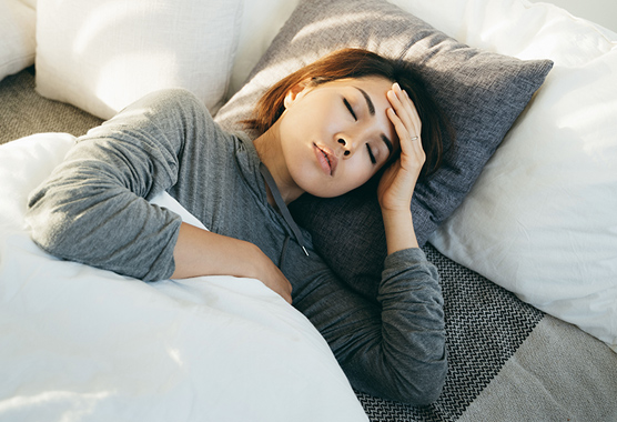 Woman lying in bed with her eyes closed and hand on her head.