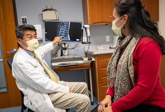 Male health care provider showing patient image of a spine on a computer screen