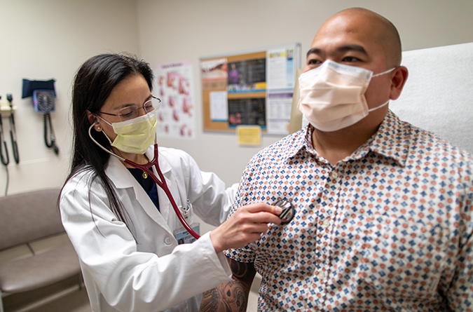 Health care provider using stethoscope to listen to male patient’s heart.