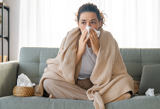 Woman sitting on a couch blowing her nose.