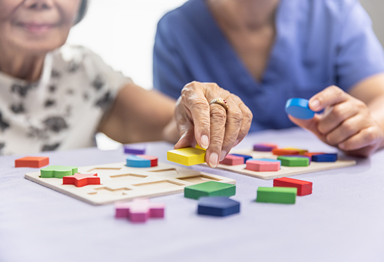 Woman with dementia working on puzzle with colorful blocks on a table.