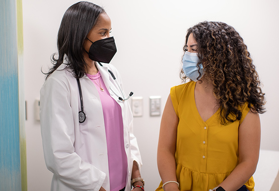 Masked healthcare worker and masked patient in a treatment room.