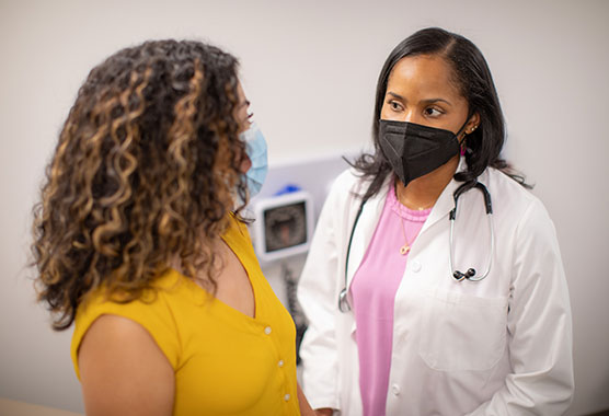 Female patient and female physician wearing masks in an exam room