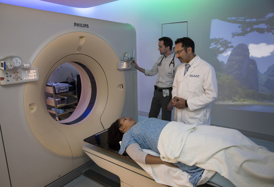 Woman getting screened for cancer with two health care providers talking to her and preparing the machine