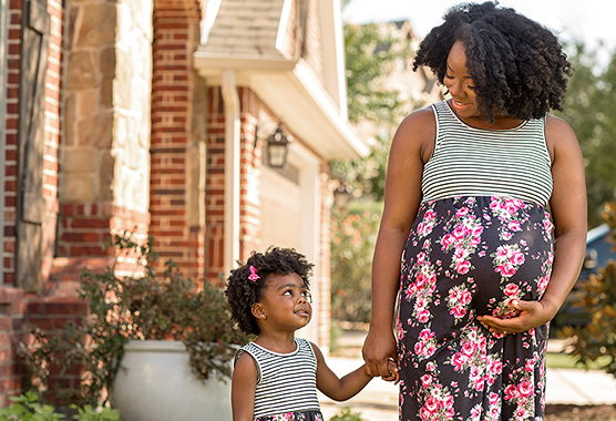 Pregnant mother and young daughter walking and holding hands.